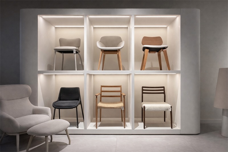 Sillas modernas tapizadas y de madera presentadas en estantería con iluminación integrada. Exposición de sillas de diseño en estantería iluminada, con modelos tapizados y de madera en diferentes estilos y acabados.