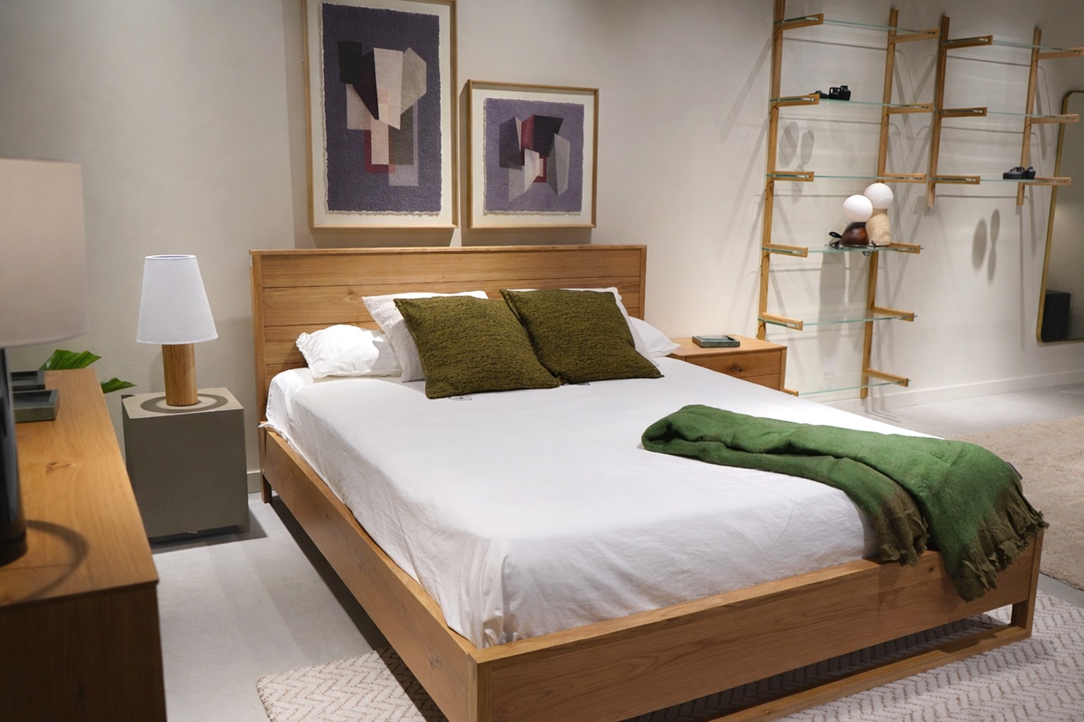 Dormitorio con cama de madera y decoración contemporánea en tonos naturales y verdes Dormitorio moderno con cama de madera, ropa de cama blanca, cojines verdes y estantería decorativa de pared