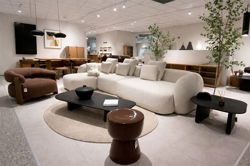 Sofá blanco de diseño curvo con mesas negras en ambiente de salón moderno. Salón contemporáneo con sofá curvo en color blanco, mesa de centro negra, mesa auxiliar y sillón tapizado en tono marrón.